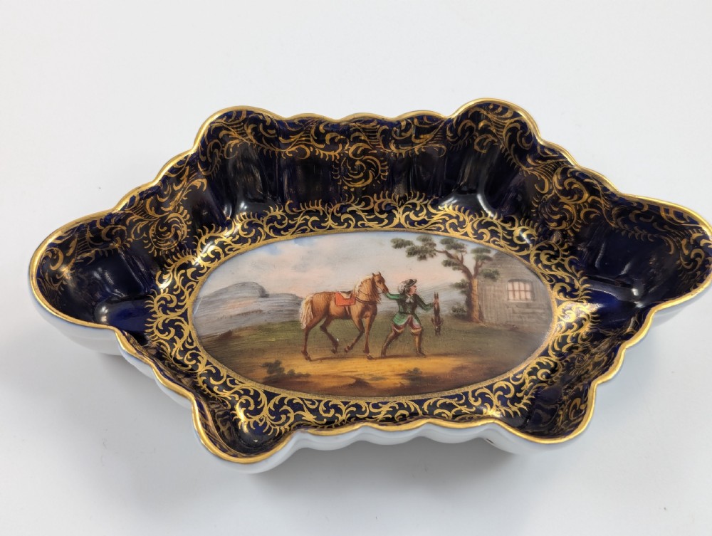 An oval lobed Dresden porcelain dish featuring a cobalt blue rim decorated with gilt scrollwork and a central hand-painted equestrian scene. View IX