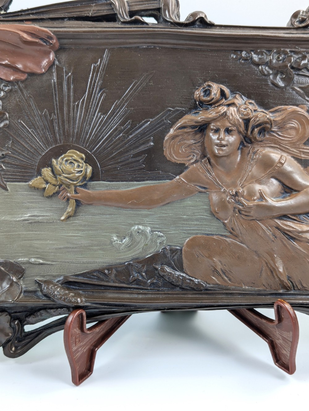 A rectangular French Art Nouveau terracotta relief featuring a draped female figure holding a rose against a rising sun background with a metallic finish. View III