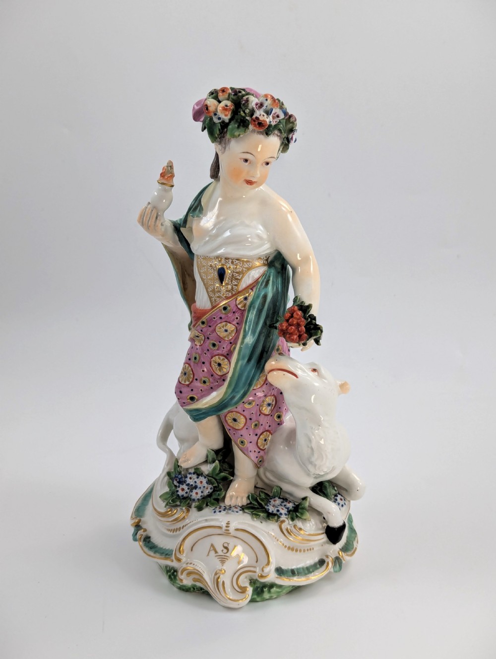 An 18th-century Derby porcelain allegorical figure depicting Asia wearing a floral crown and patterned pink drapery alongside a camel on a scrollwork base.