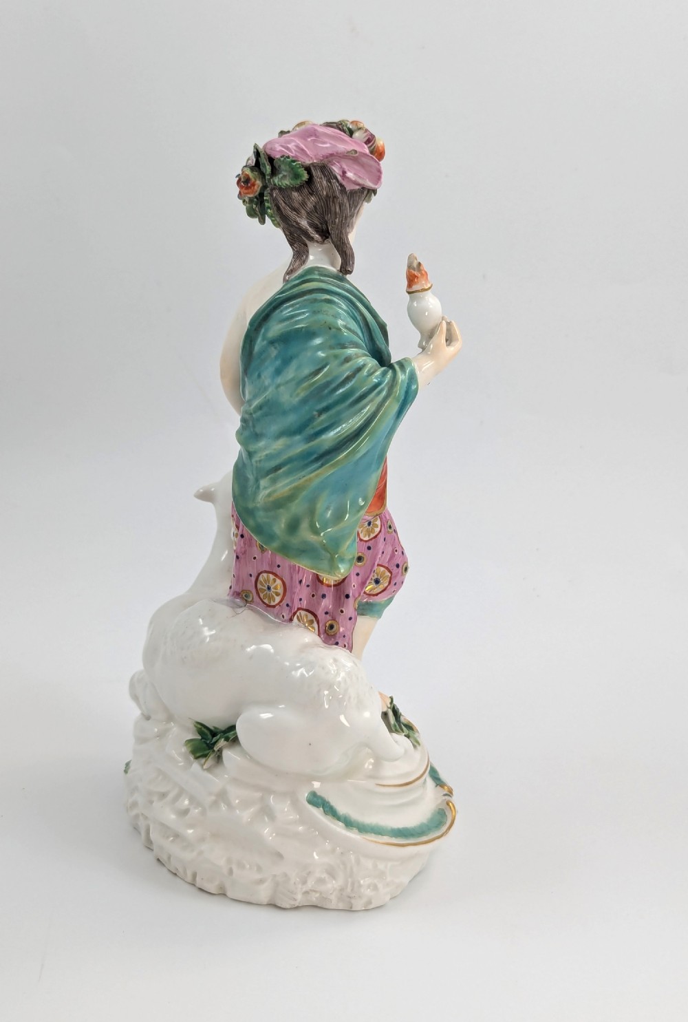 An 18th-century Derby porcelain allegorical figure depicting Asia wearing a floral crown and patterned pink drapery alongside a camel on a scrollwork base. View V