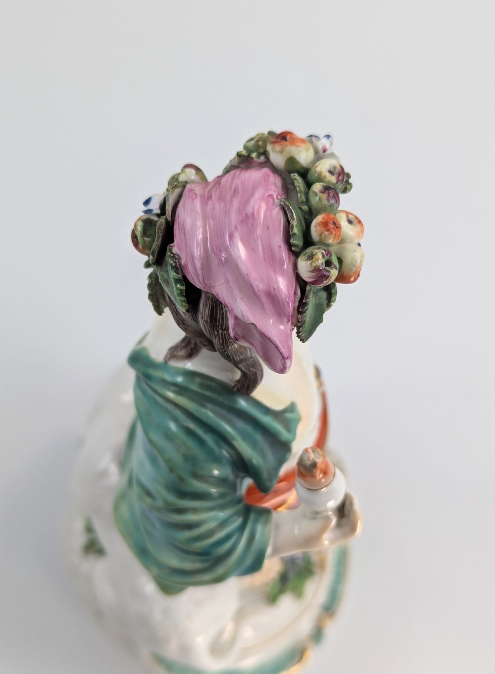 An 18th-century Derby porcelain allegorical figure depicting Asia wearing a floral crown and patterned pink drapery alongside a camel on a scrollwork base. View IX