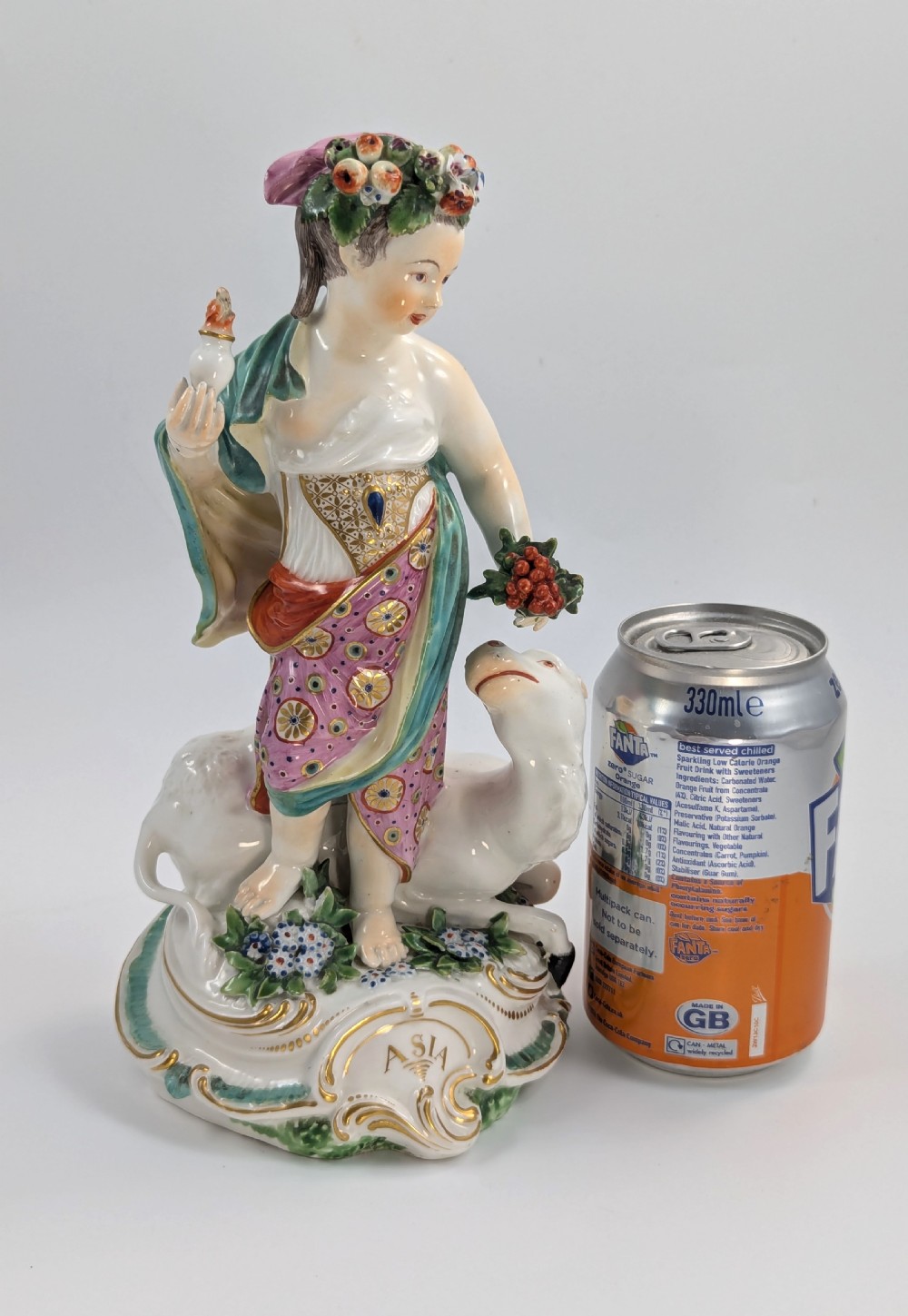 An 18th-century Derby porcelain allegorical figure depicting Asia wearing a floral crown and patterned pink drapery alongside a camel on a scrollwork base. View XI