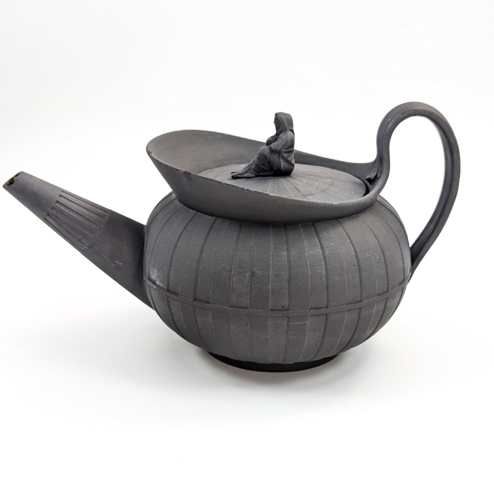 An eighteenth-century Wedgwood black basalt teapot featuring a ribbed stoneware body, high loop handle, and a seated female figure finial on the lid.