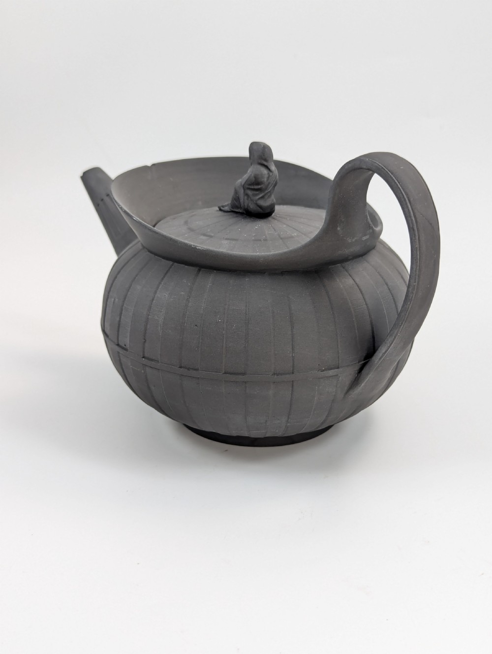 An eighteenth-century Wedgwood black basalt teapot featuring a ribbed stoneware body, high loop handle, and a seated female figure finial on the lid. View III