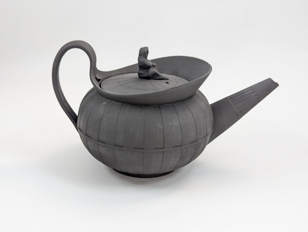 An eighteenth-century Wedgwood black basalt teapot featuring a ribbed stoneware body, high loop handle, and a seated female figure finial on the lid. View VI