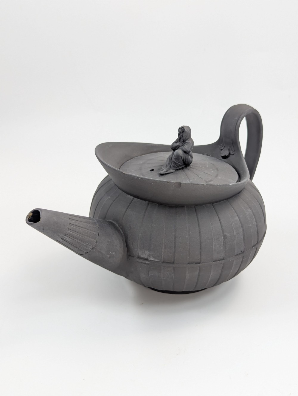 An eighteenth-century Wedgwood black basalt teapot featuring a ribbed stoneware body, high loop handle, and a seated female figure finial on the lid. View VIII