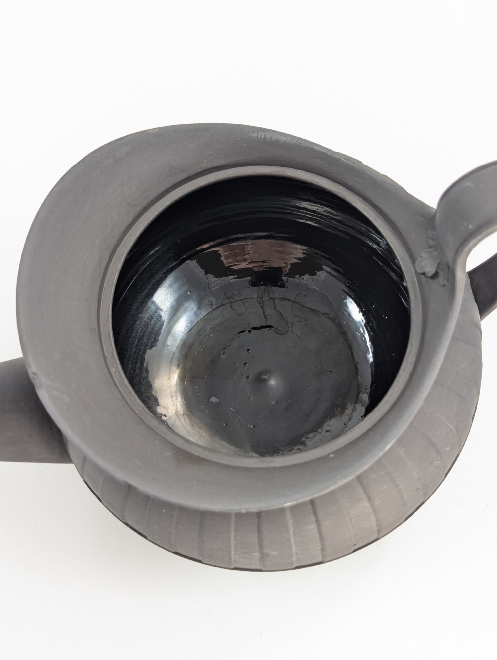 An eighteenth-century Wedgwood black basalt teapot featuring a ribbed stoneware body, high loop handle, and a seated female figure finial on the lid. View X
