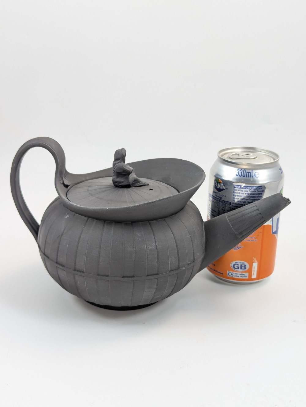 An eighteenth-century Wedgwood black basalt teapot featuring a ribbed stoneware body, high loop handle, and a seated female figure finial on the lid. View XIV