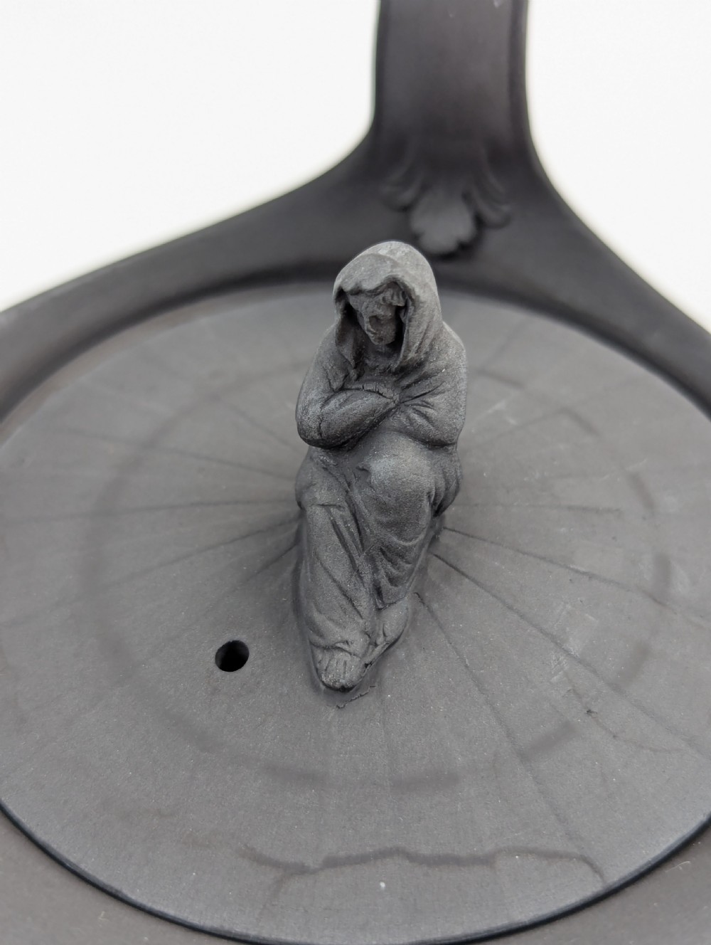 An eighteenth-century Wedgwood black basalt teapot featuring a ribbed stoneware body, high loop handle, and a seated female figure finial on the lid. View XV