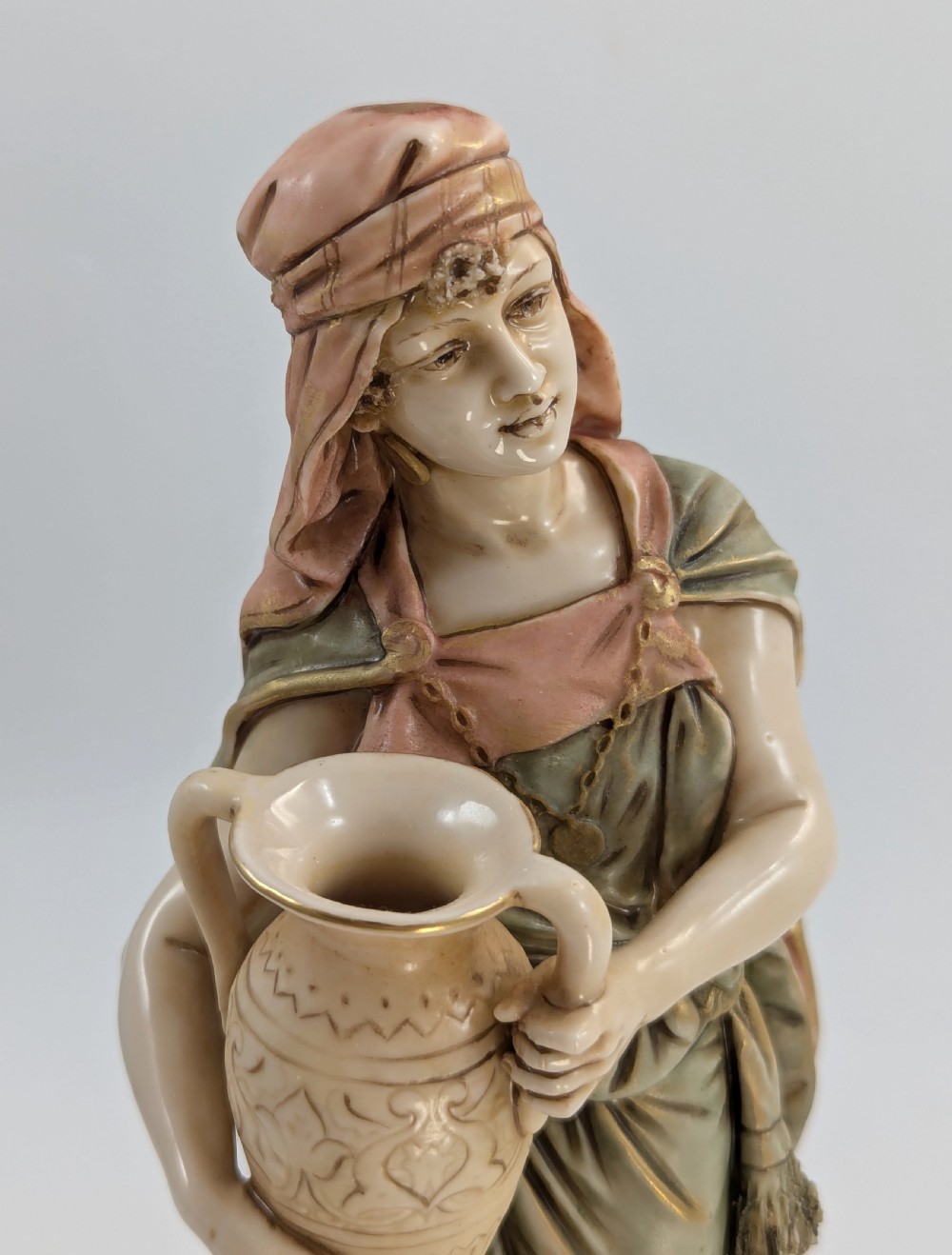 A porcelain figurine of a woman in draped robes carrying a double-handled water vessel on a patterned pedestal base. View VIII