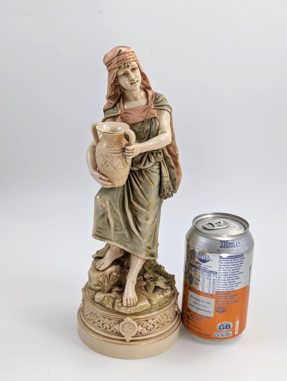 A porcelain figurine of a woman in draped robes carrying a double-handled water vessel on a patterned pedestal base. View IX
