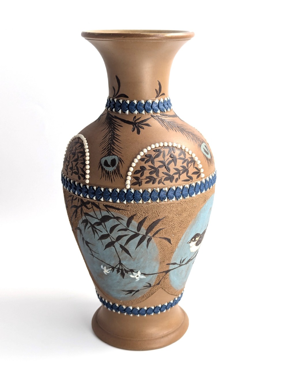 A late 19th-century stoneware vase featuring a flared rim, warm brown buff body decorated with raised blue and white beaded borders, peacock feather motifs, and a painted central oval panel displaying a bird. View III