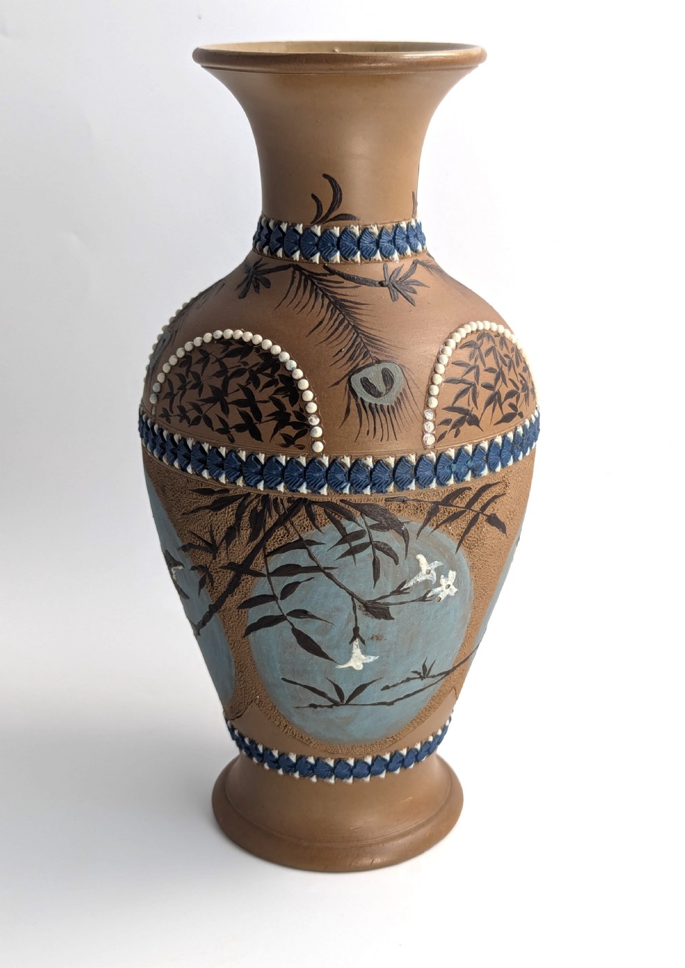 A late 19th-century stoneware vase featuring a flared rim, warm brown buff body decorated with raised blue and white beaded borders, peacock feather motifs, and a painted central oval panel displaying a bird. View VI