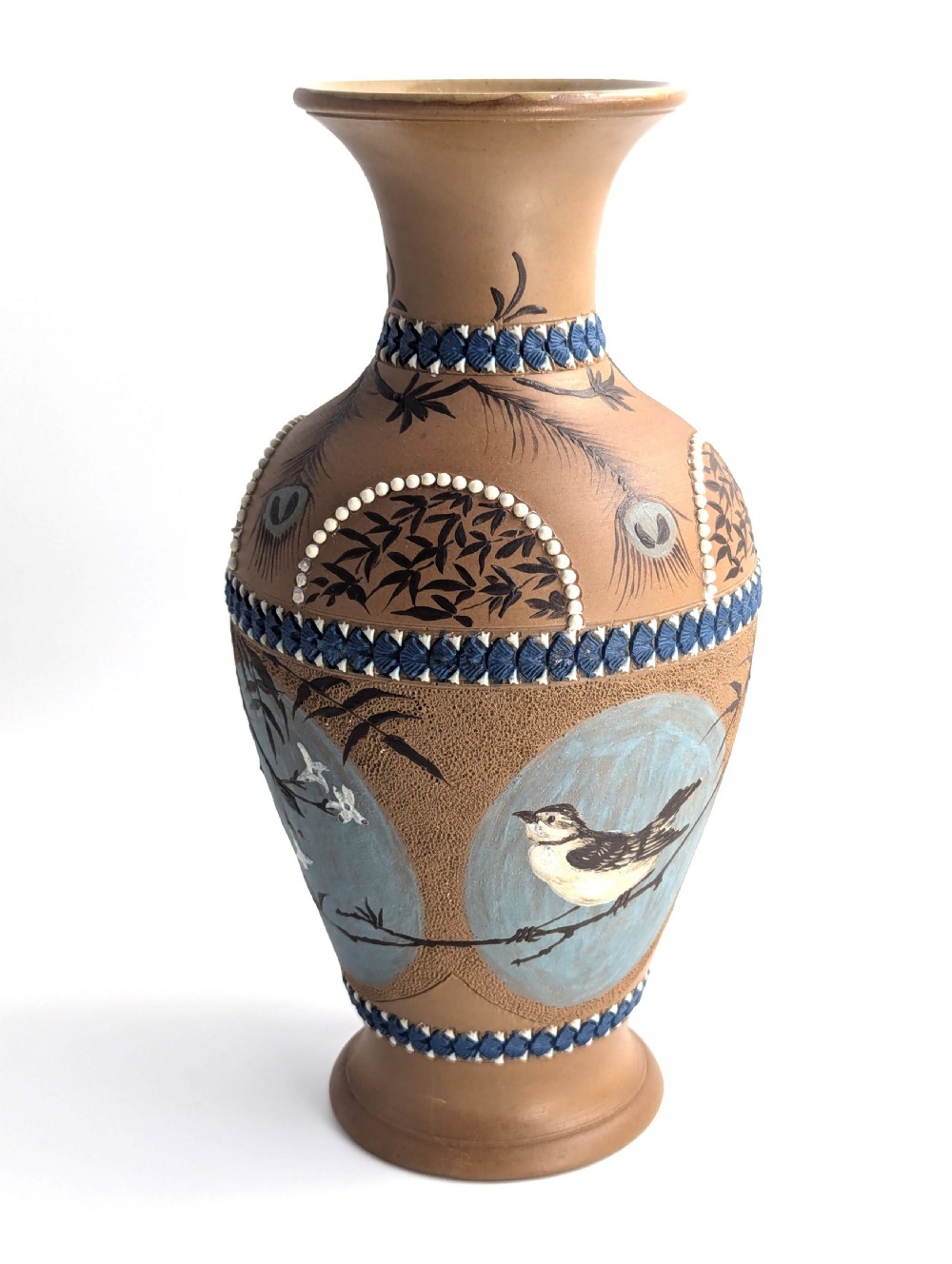 A late 19th-century stoneware vase featuring a flared rim, warm brown buff body decorated with raised blue and white beaded borders, peacock feather motifs, and a painted central oval panel displaying a bird. View VII