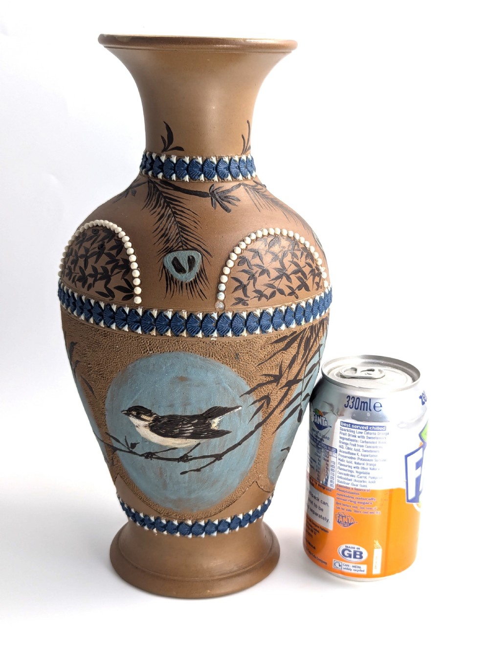 A late 19th-century stoneware vase featuring a flared rim, warm brown buff body decorated with raised blue and white beaded borders, peacock feather motifs, and a painted central oval panel displaying a bird. View X