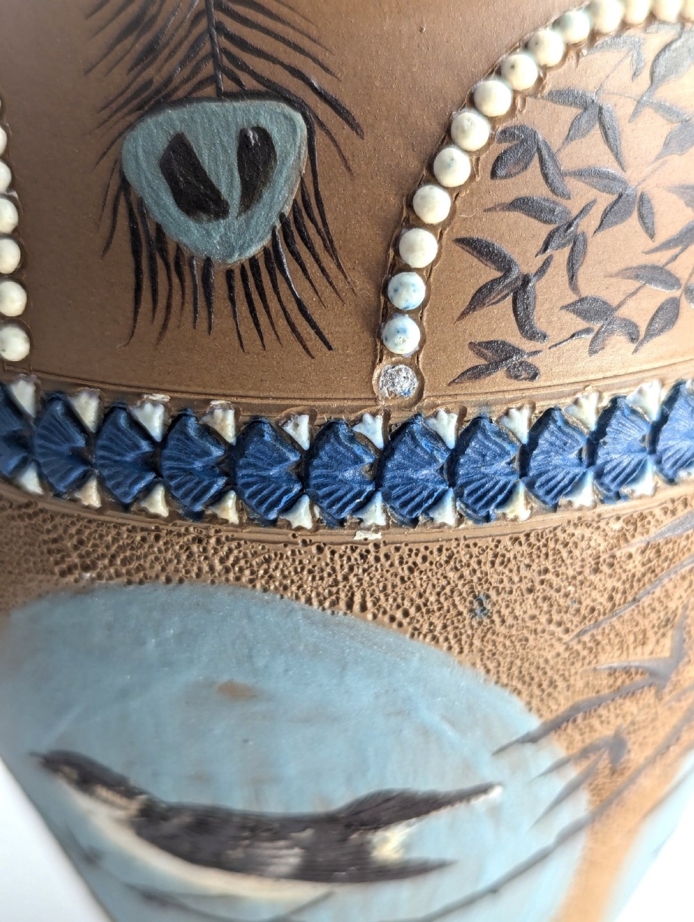 A late 19th-century stoneware vase featuring a flared rim, warm brown buff body decorated with raised blue and white beaded borders, peacock feather motifs, and a painted central oval panel displaying a bird. View XII
