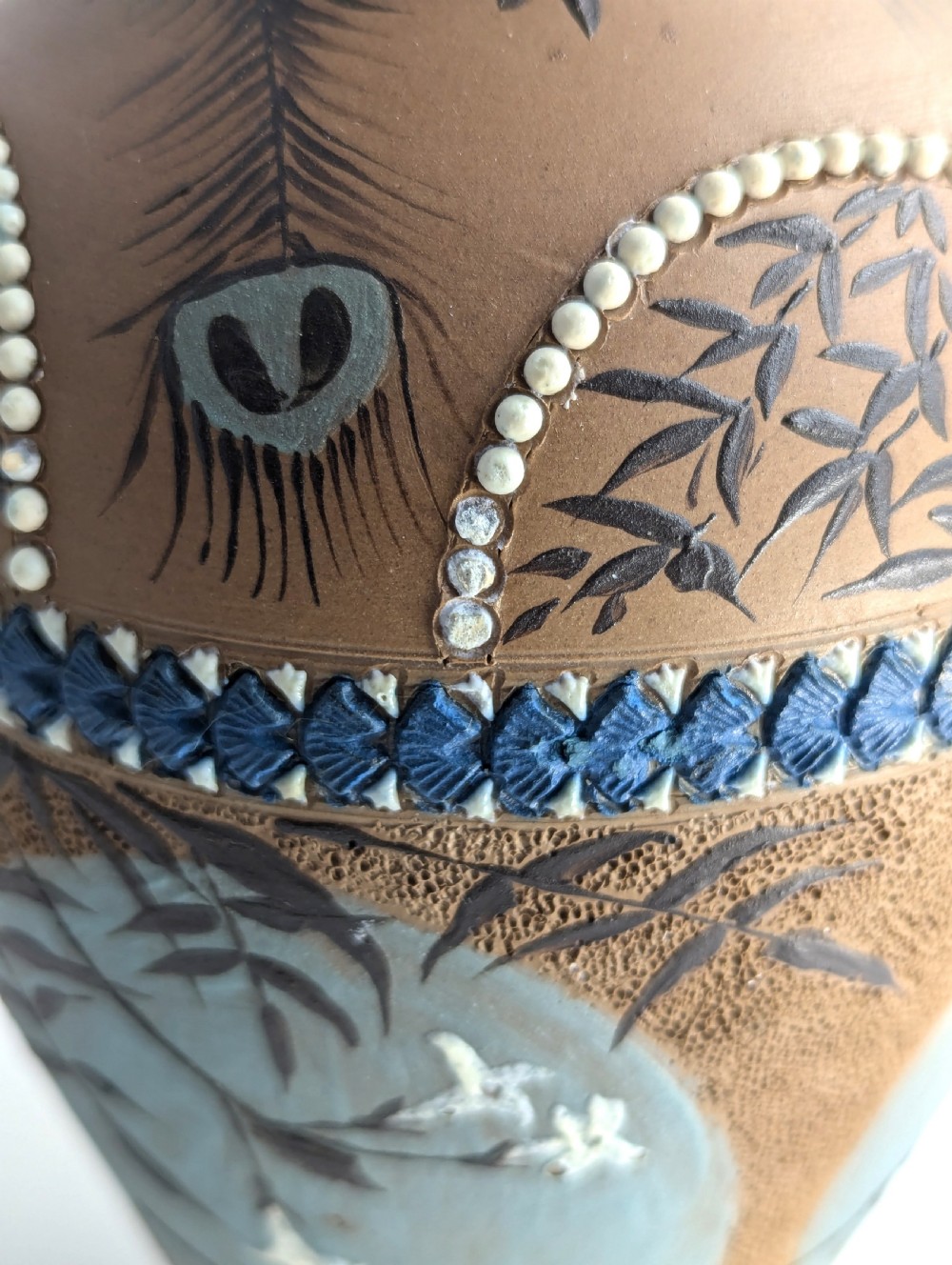 A late 19th-century stoneware vase featuring a flared rim, warm brown buff body decorated with raised blue and white beaded borders, peacock feather motifs, and a painted central oval panel displaying a bird. View XIII