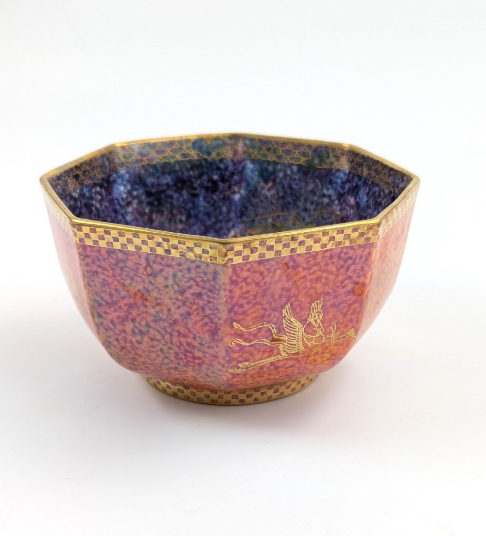 An octagonal Art Deco porcelain bowl featuring a mottled pink exterior with gold mythological motifs and an iridescent blue interior bounded by a gilded checkered rim.