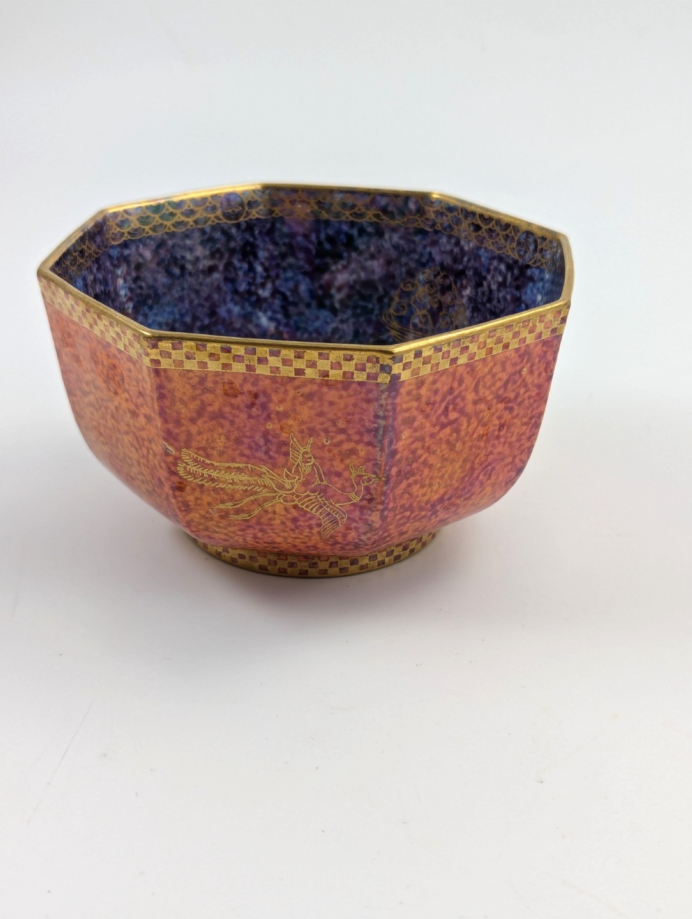 An octagonal Art Deco porcelain bowl featuring a mottled pink exterior with gold mythological motifs and an iridescent blue interior bounded by a gilded checkered rim. View III