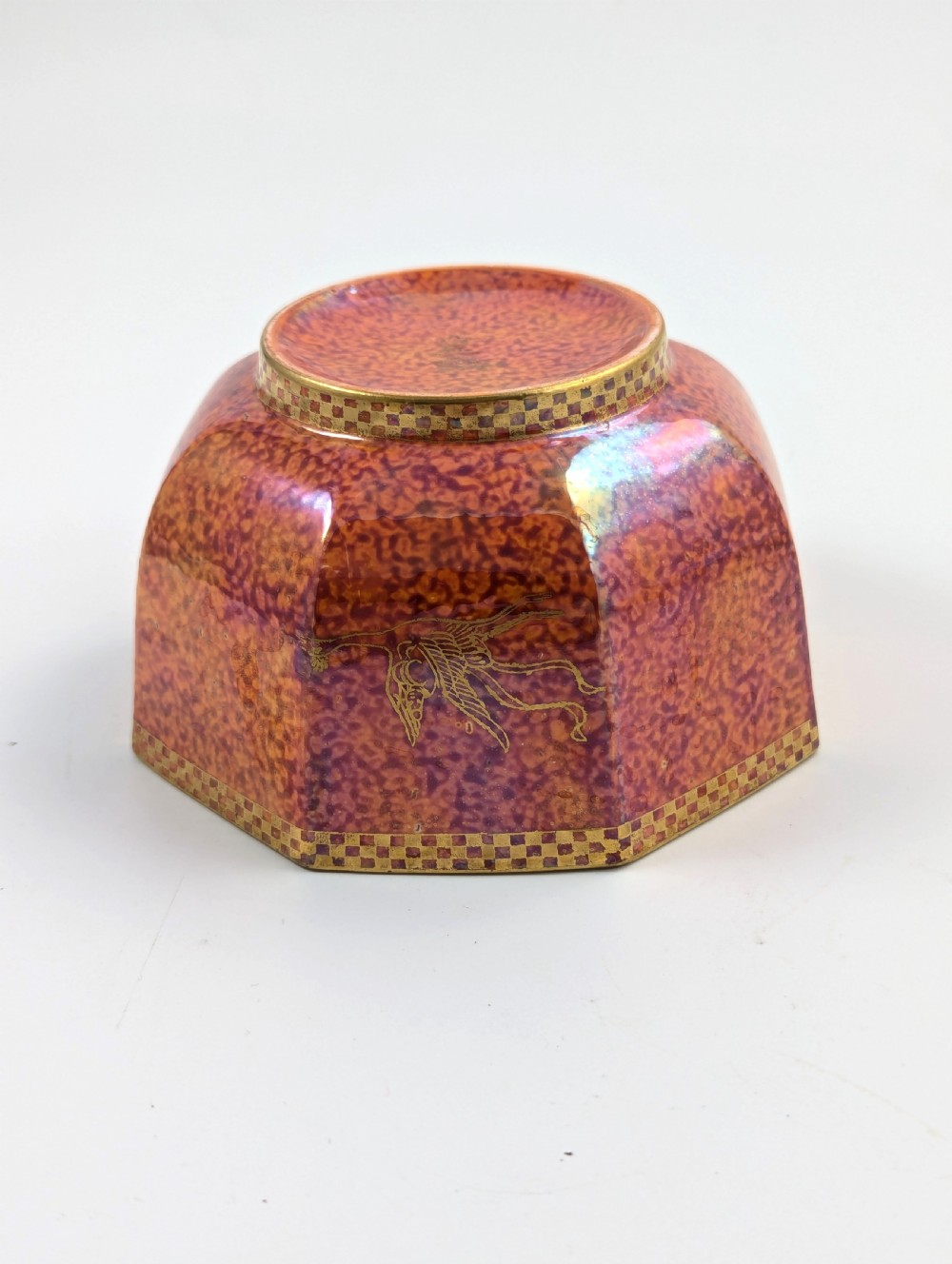 An octagonal Art Deco porcelain bowl featuring a mottled pink exterior with gold mythological motifs and an iridescent blue interior bounded by a gilded checkered rim. View IV