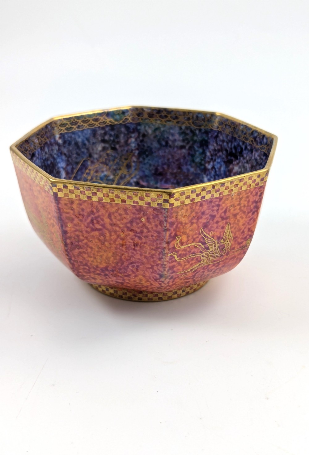 An octagonal Art Deco porcelain bowl featuring a mottled pink exterior with gold mythological motifs and an iridescent blue interior bounded by a gilded checkered rim. View VI