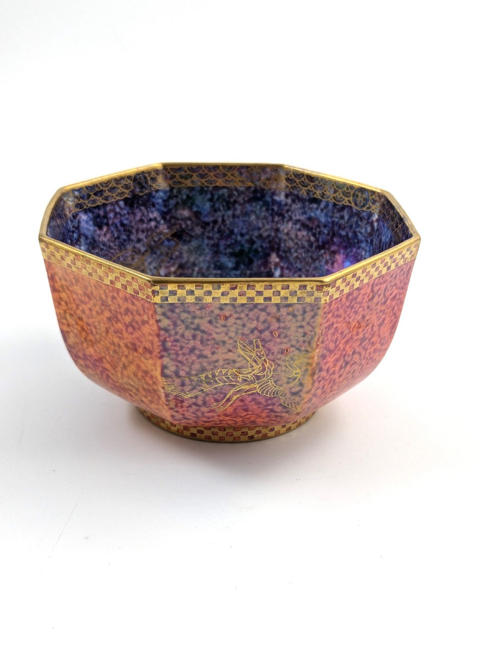 An octagonal Art Deco porcelain bowl featuring a mottled pink exterior with gold mythological motifs and an iridescent blue interior bounded by a gilded checkered rim. View VII