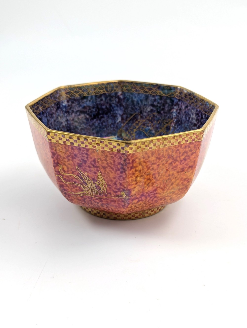 An octagonal Art Deco porcelain bowl featuring a mottled pink exterior with gold mythological motifs and an iridescent blue interior bounded by a gilded checkered rim. View IX