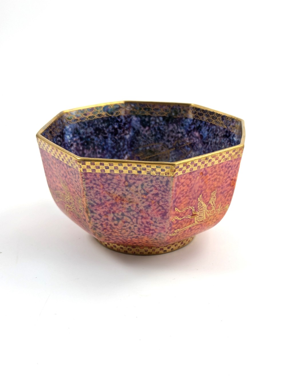 An octagonal Art Deco porcelain bowl featuring a mottled pink exterior with gold mythological motifs and an iridescent blue interior bounded by a gilded checkered rim. View X