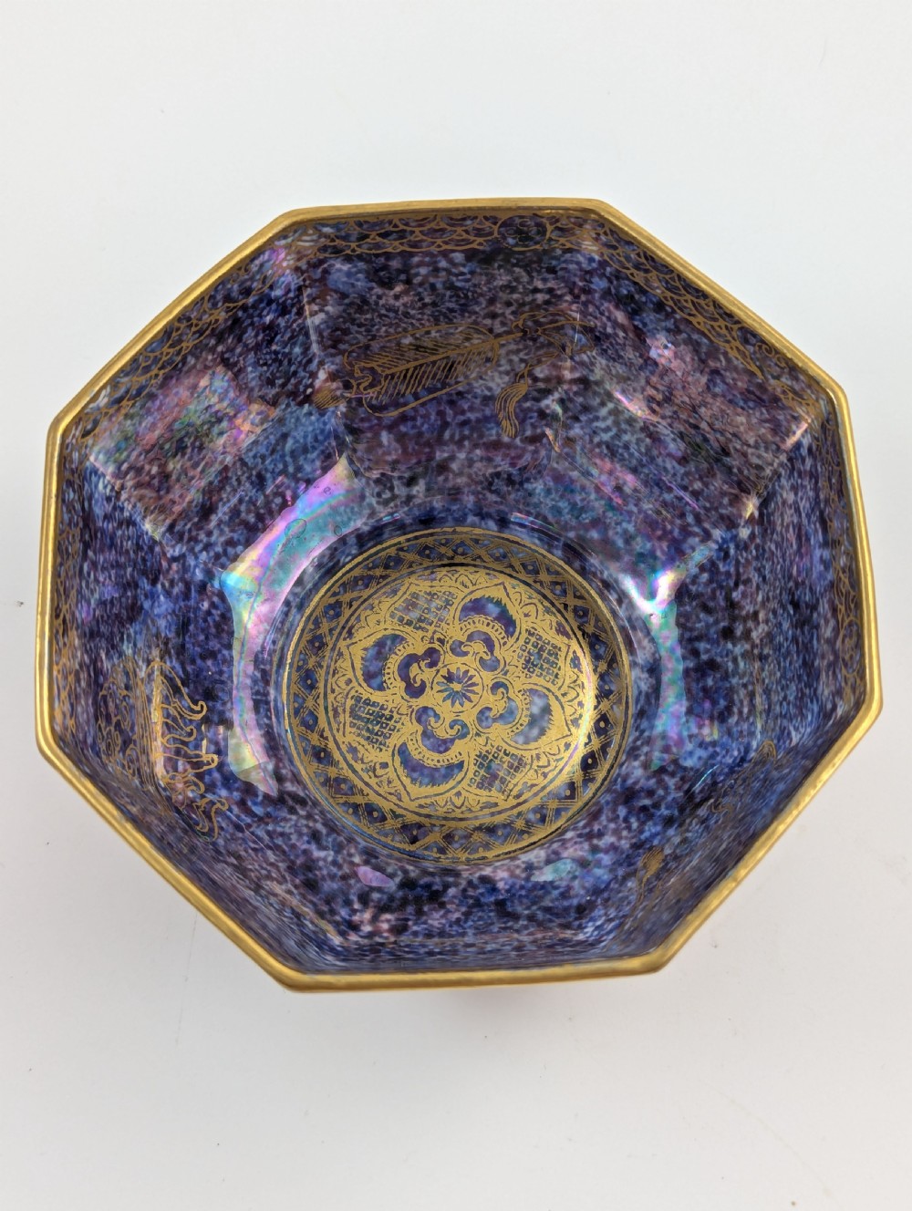An octagonal Art Deco porcelain bowl featuring a mottled pink exterior with gold mythological motifs and an iridescent blue interior bounded by a gilded checkered rim. View XI