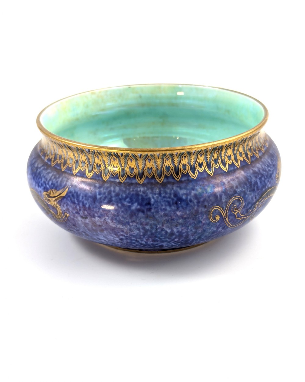 A rounded ceramic bowl featuring a mottled blue exterior decorated with a gilded dragon motif, a gilt patterned rim, and a pale iridescent green interior glaze. View II