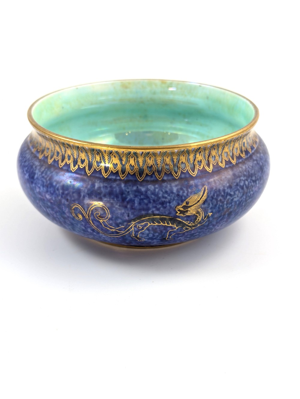 A rounded ceramic bowl featuring a mottled blue exterior decorated with a gilded dragon motif, a gilt patterned rim, and a pale iridescent green interior glaze. View III