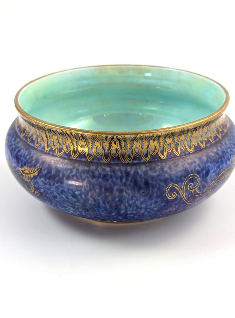 A rounded ceramic bowl featuring a mottled blue exterior decorated with a gilded dragon motif, a gilt patterned rim, and a pale iridescent green interior glaze. View VIII