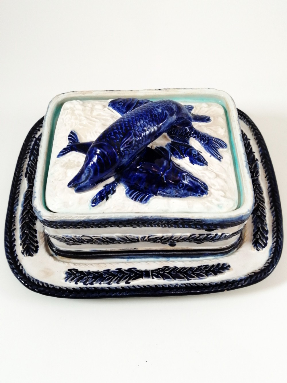 A rectangular Victorian majolica sardine box with matching undertray featuring cobalt blue fish relief decoration on an off-white lid.