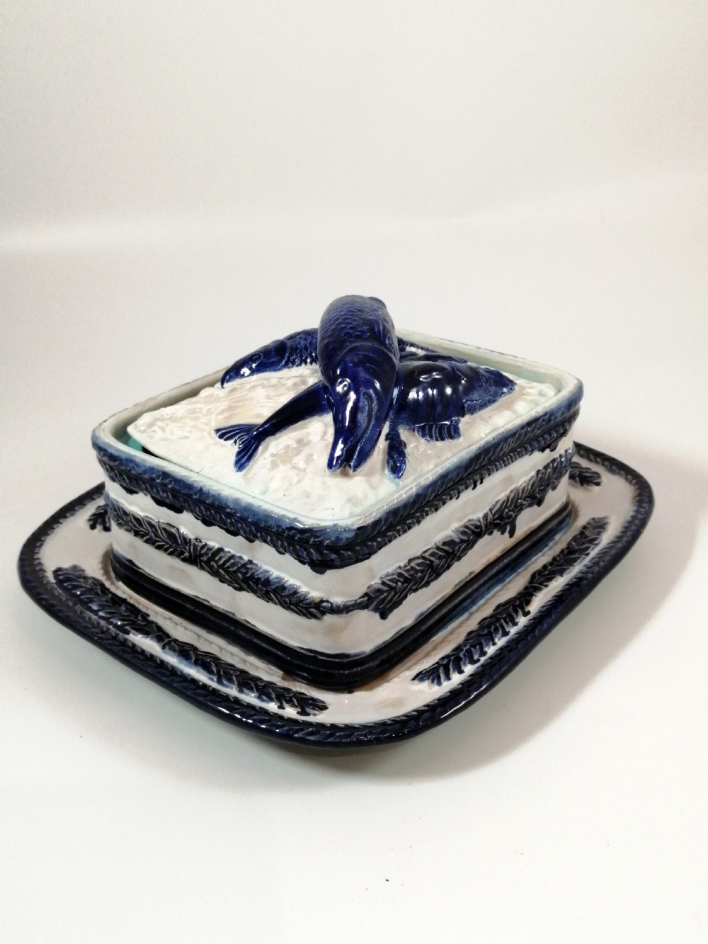 A rectangular Victorian majolica sardine box with matching undertray featuring cobalt blue fish relief decoration on an off-white lid. View II