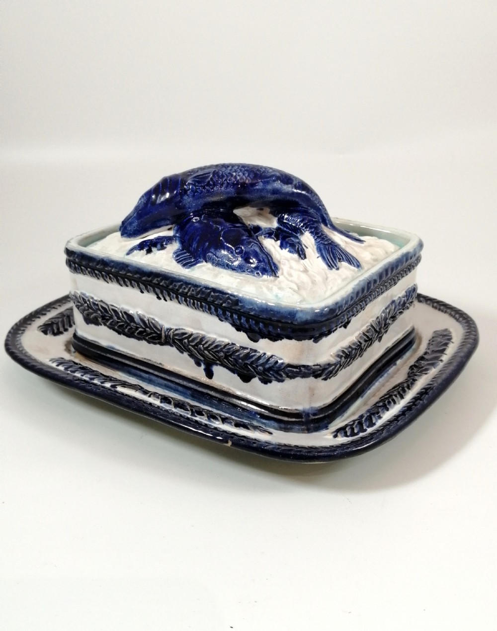 A rectangular Victorian majolica sardine box with matching undertray featuring cobalt blue fish relief decoration on an off-white lid. View IV