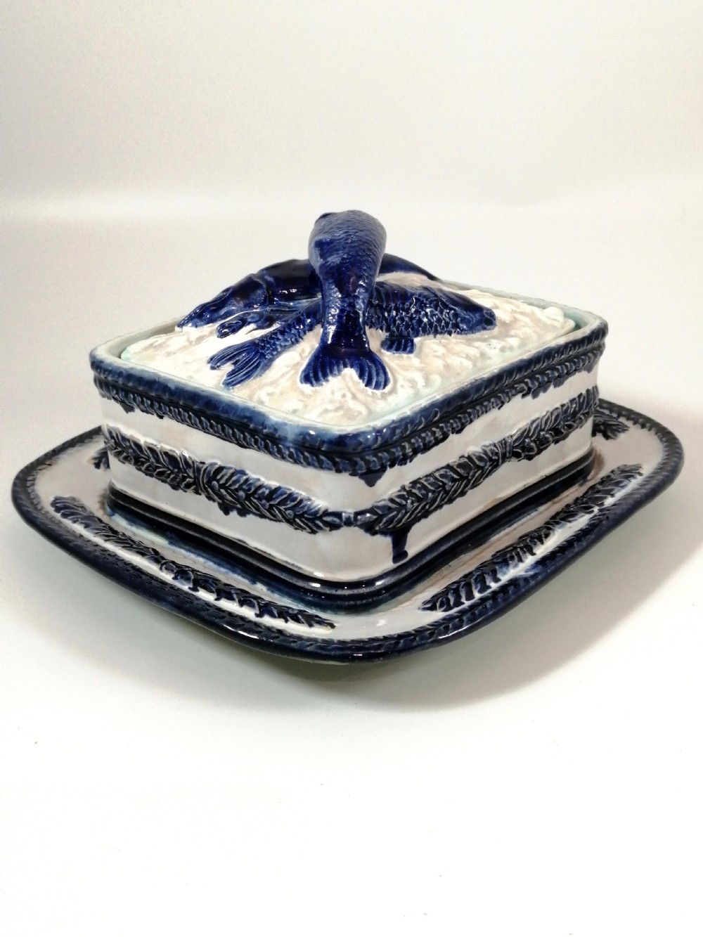A rectangular Victorian majolica sardine box with matching undertray featuring cobalt blue fish relief decoration on an off-white lid. View VI