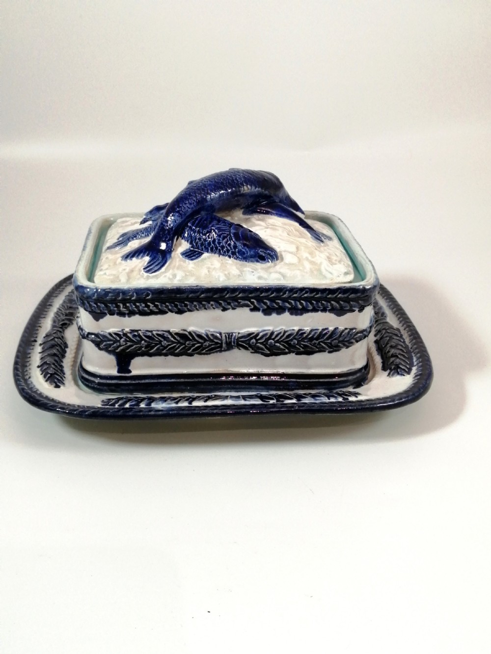 A rectangular Victorian majolica sardine box with matching undertray featuring cobalt blue fish relief decoration on an off-white lid. View VII