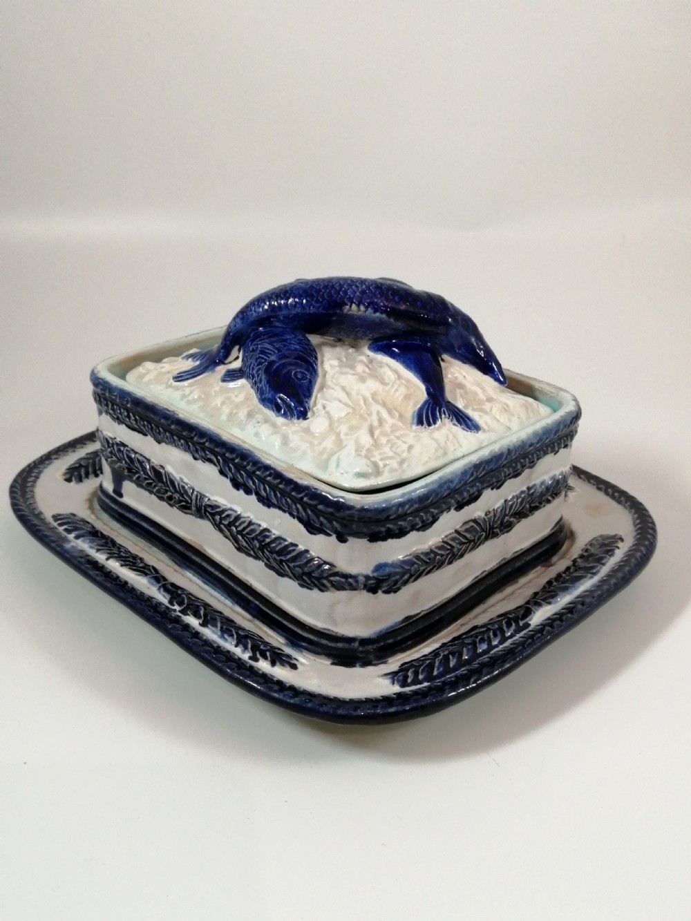A rectangular Victorian majolica sardine box with matching undertray featuring cobalt blue fish relief decoration on an off-white lid. View VIII