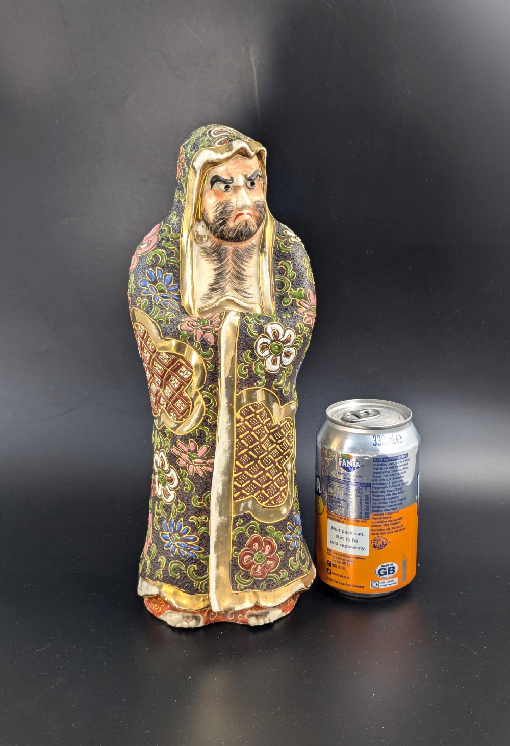 A Japanese Satsuma earthenware figurine depicting a bearded Daruma monk wearing a hooded robe with polychrome enamels and gold accents. View IX
