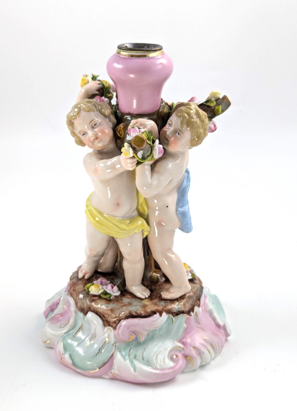 A 19th-century German hard-paste porcelain candlestick featuring two sculpted cherubs around a central column on a pastel Rococo scroll base.