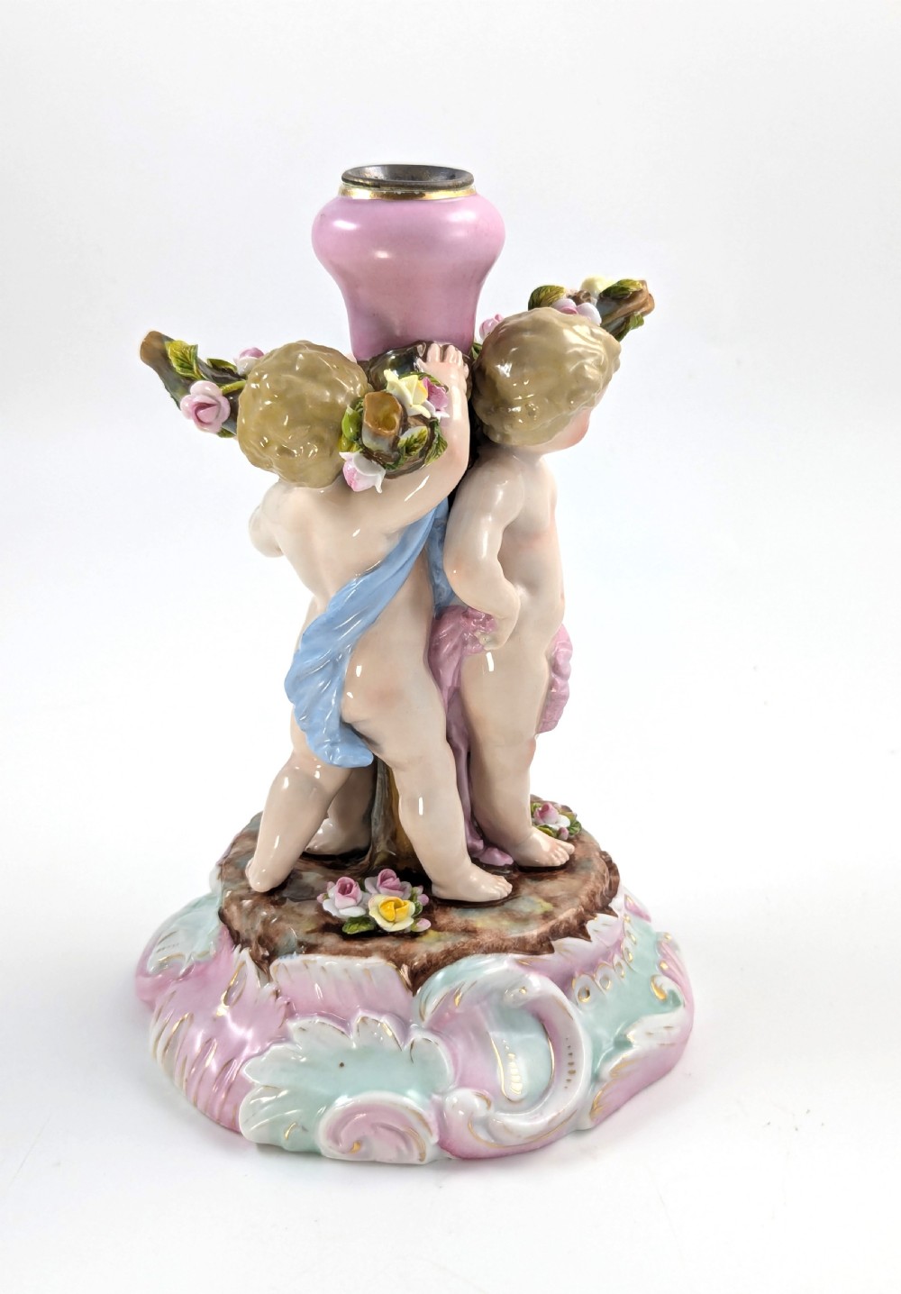 A 19th-century German hard-paste porcelain candlestick featuring two sculpted cherubs around a central column on a pastel Rococo scroll base. View III