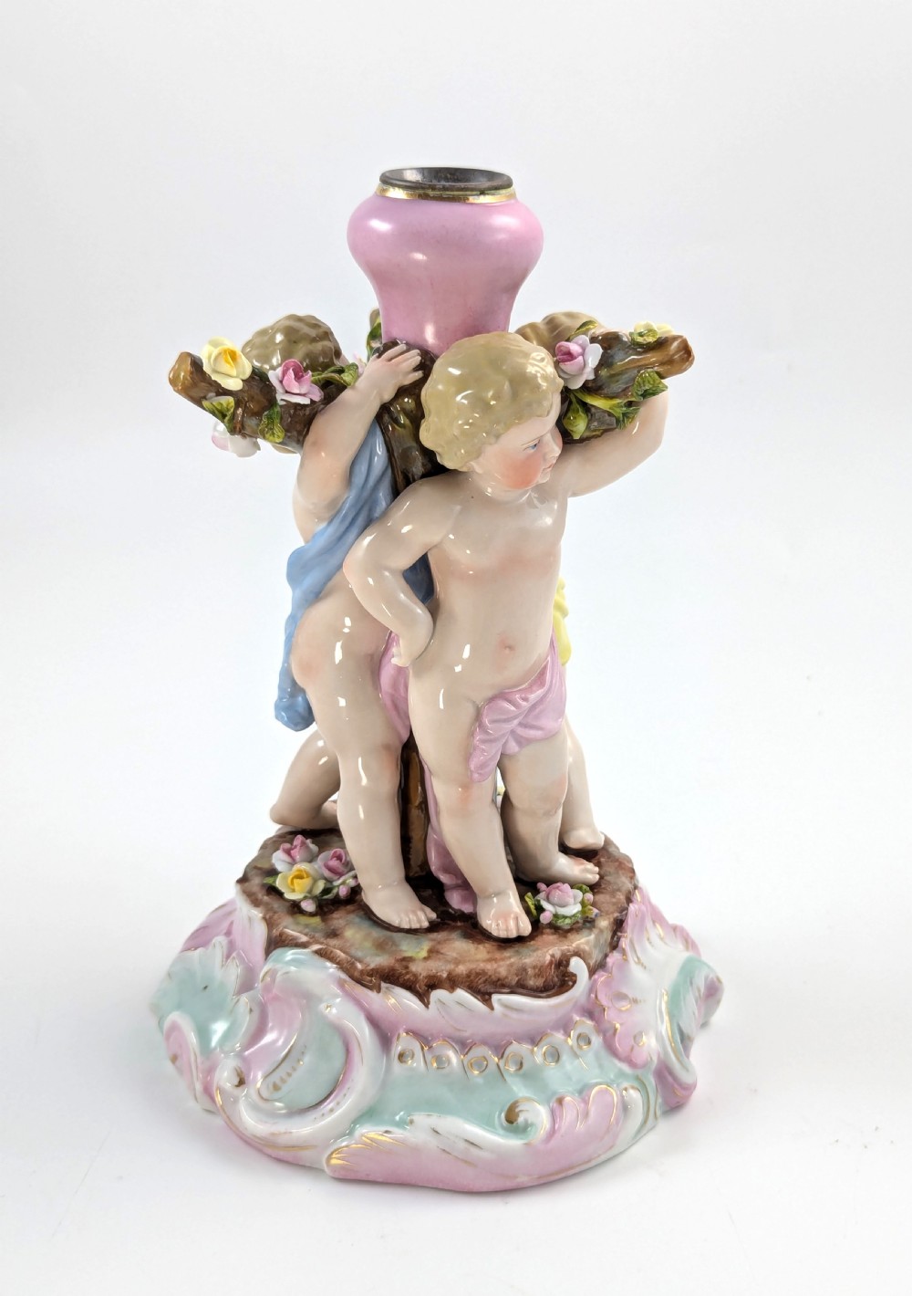 A 19th-century German hard-paste porcelain candlestick featuring two sculpted cherubs around a central column on a pastel Rococo scroll base. View IV
