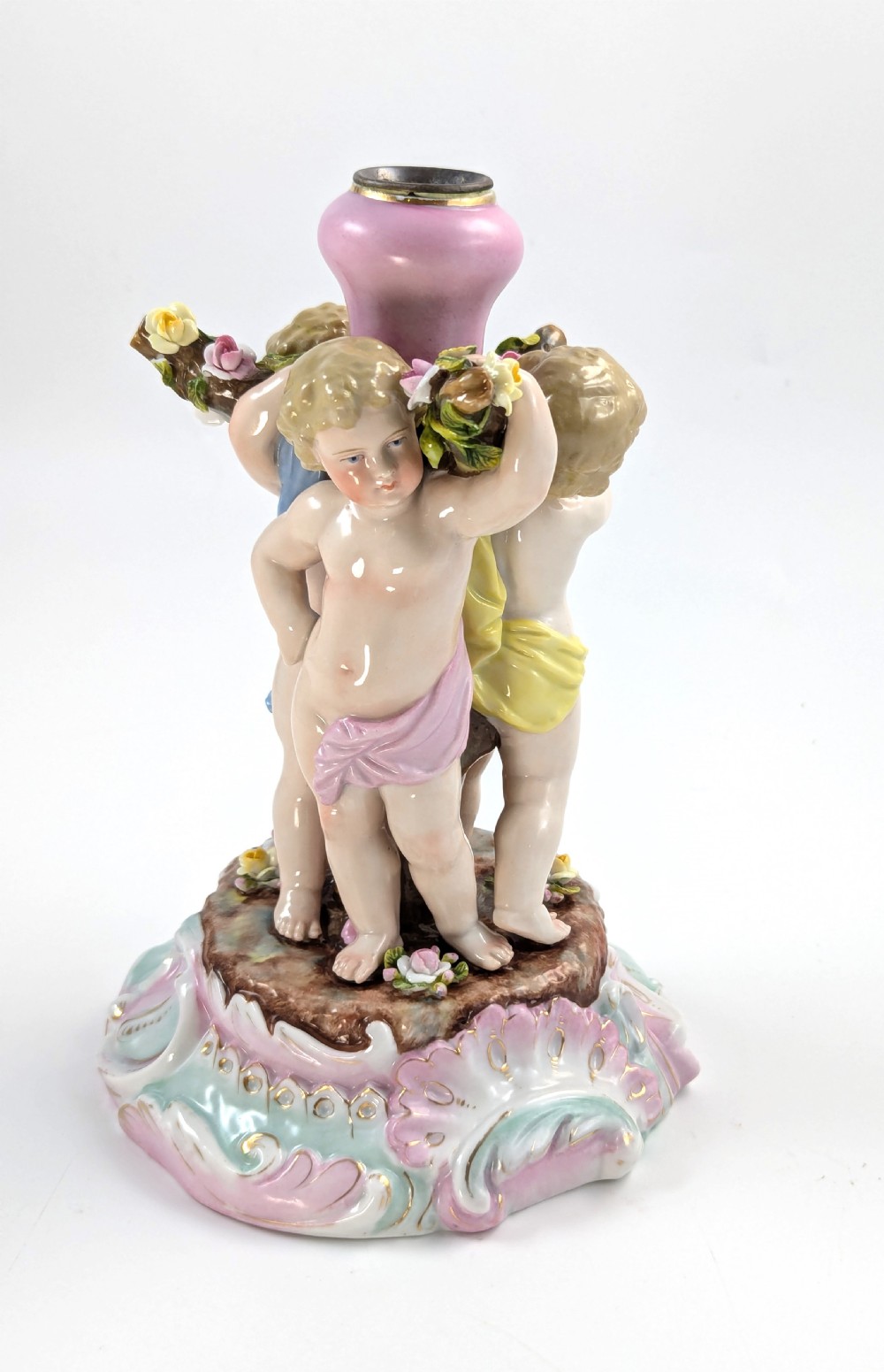 A 19th-century German hard-paste porcelain candlestick featuring two sculpted cherubs around a central column on a pastel Rococo scroll base. View V