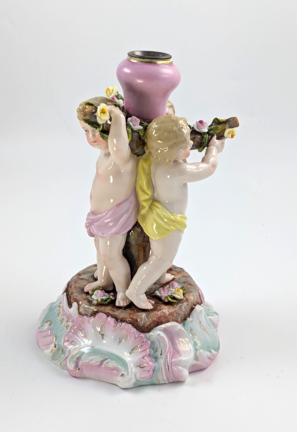 A 19th-century German hard-paste porcelain candlestick featuring two sculpted cherubs around a central column on a pastel Rococo scroll base. View VI