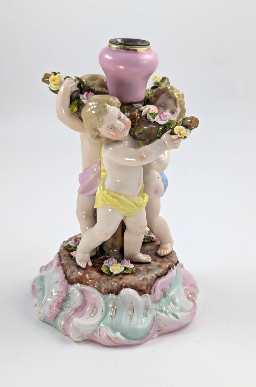 A 19th-century German hard-paste porcelain candlestick featuring two sculpted cherubs around a central column on a pastel Rococo scroll base. View VII