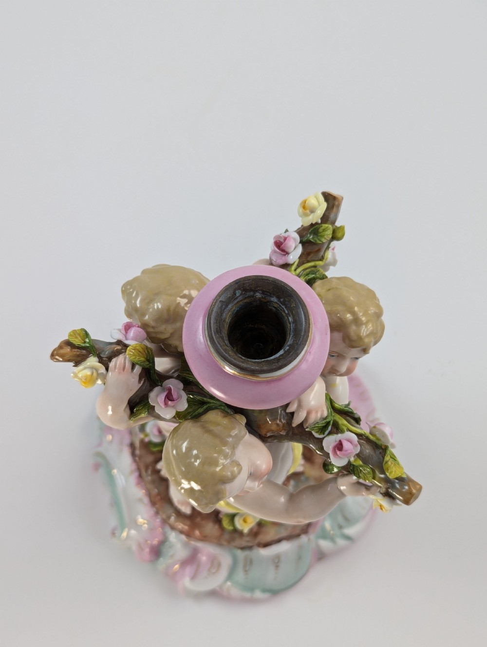 A 19th-century German hard-paste porcelain candlestick featuring two sculpted cherubs around a central column on a pastel Rococo scroll base. View VIII