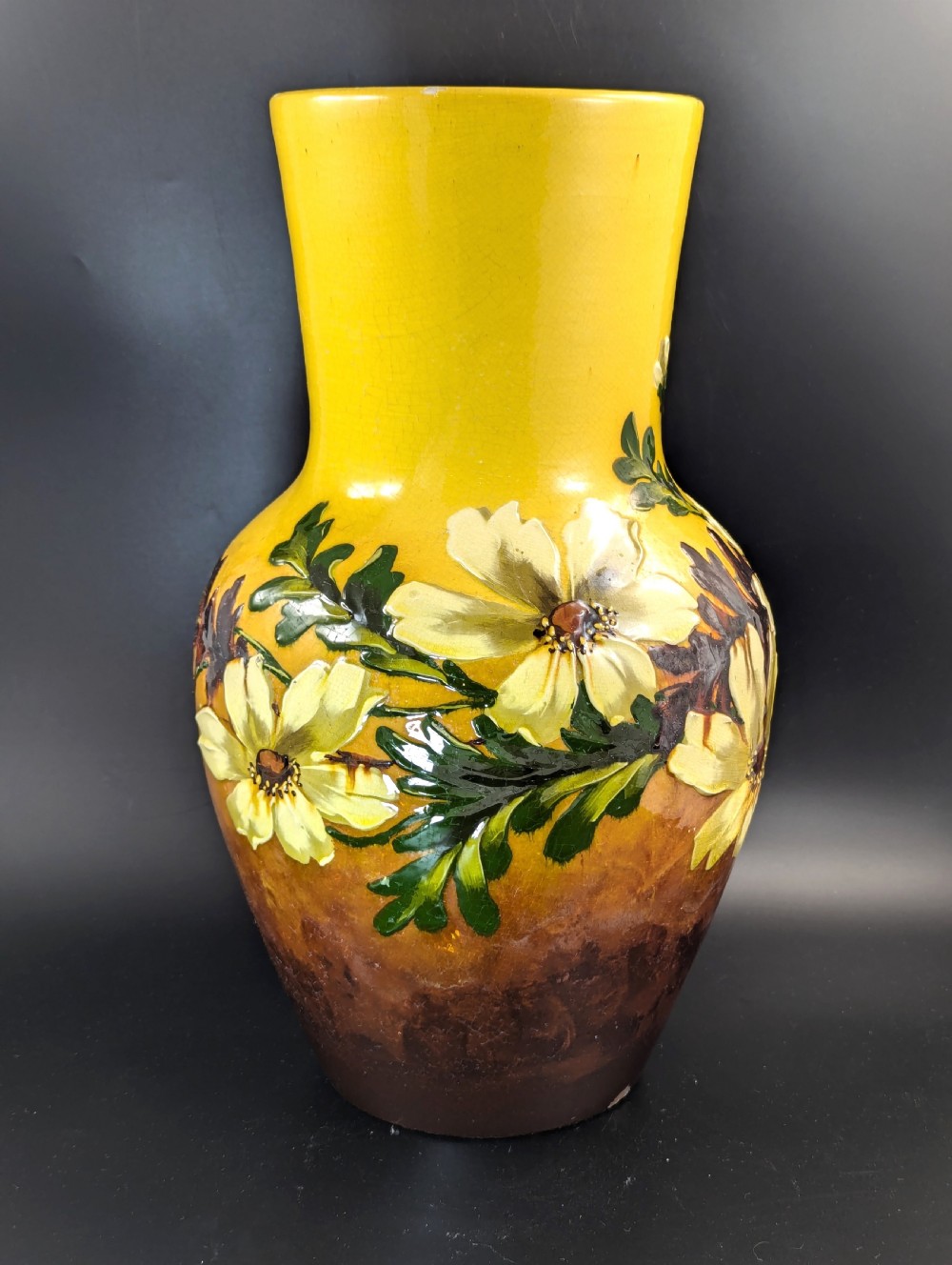 A tall ceramic vase featuring a yellow neck and upper body with raised impasto floral decoration transitioning into a dark brown glazed base. View III