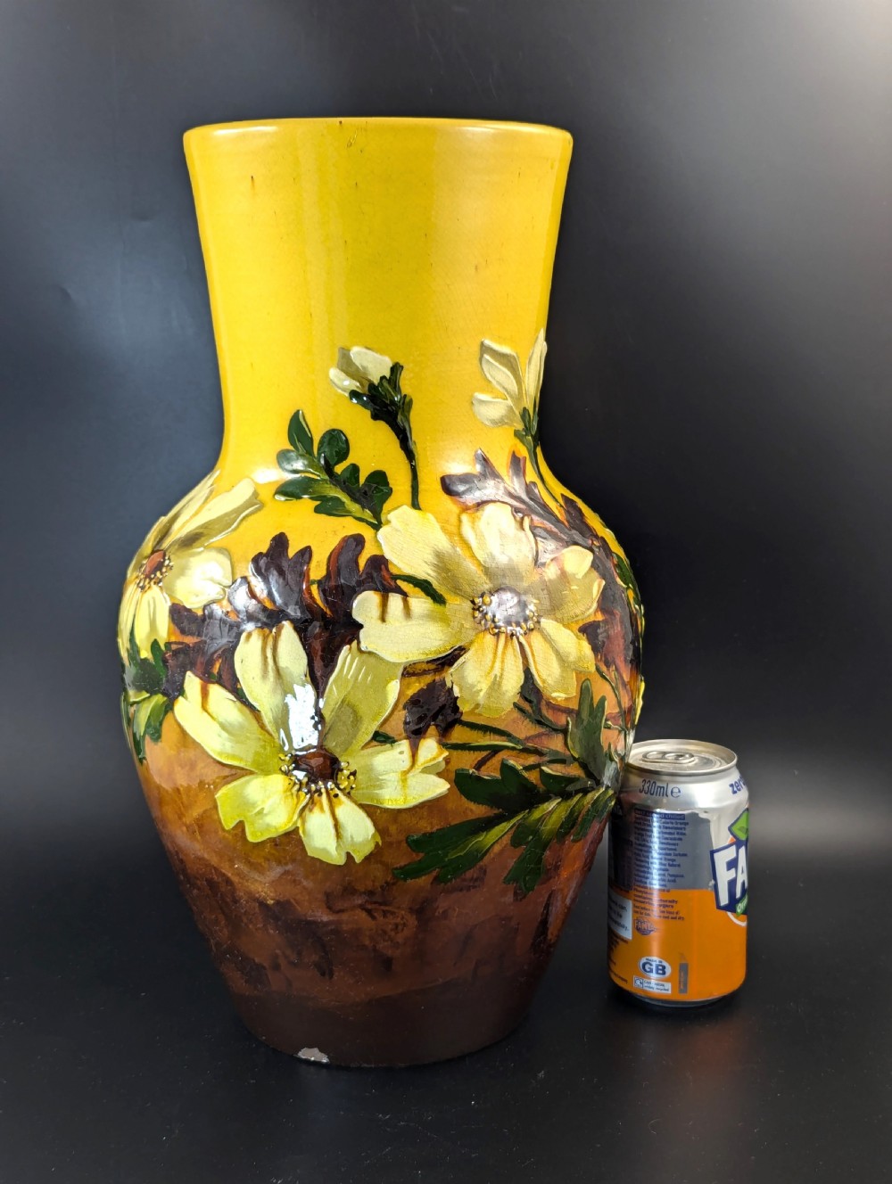 A tall ceramic vase featuring a yellow neck and upper body with raised impasto floral decoration transitioning into a dark brown glazed base. View VII