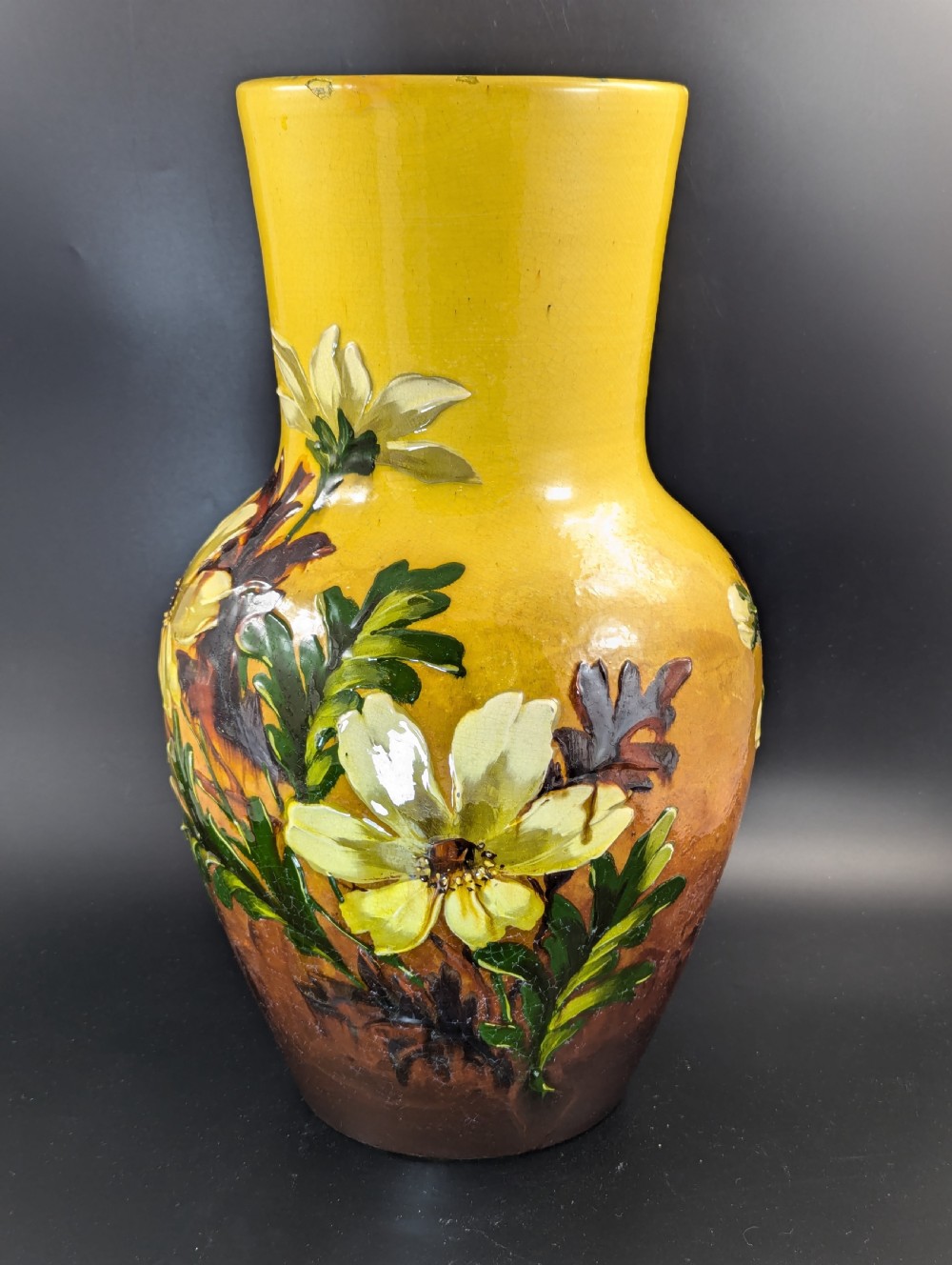A tall ceramic vase featuring a yellow neck and upper body with raised impasto floral decoration transitioning into a dark brown glazed base. View VIII