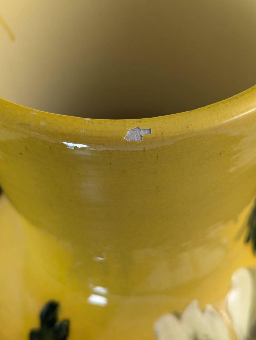 A tall ceramic vase featuring a yellow neck and upper body with raised impasto floral decoration transitioning into a dark brown glazed base. View X